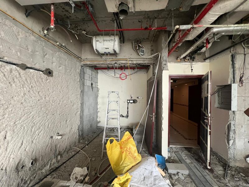 Kitchen side stripped to the structure with services exposed, apartment entrance door open on the right