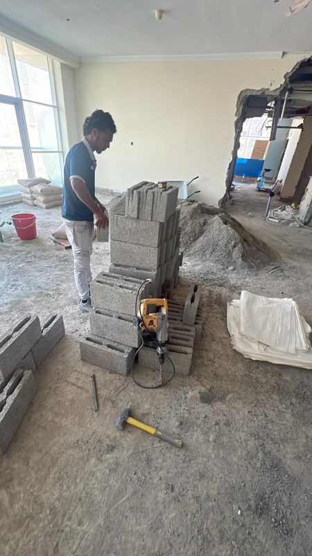 Team member stacking blocks in the living area during strip-out, wall opened on the right for the corridor