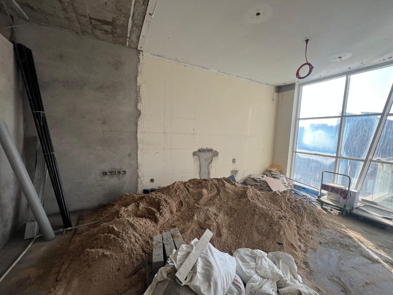 TV wall being set out in pencil beside full-height glazing, sand stockpiled for the works